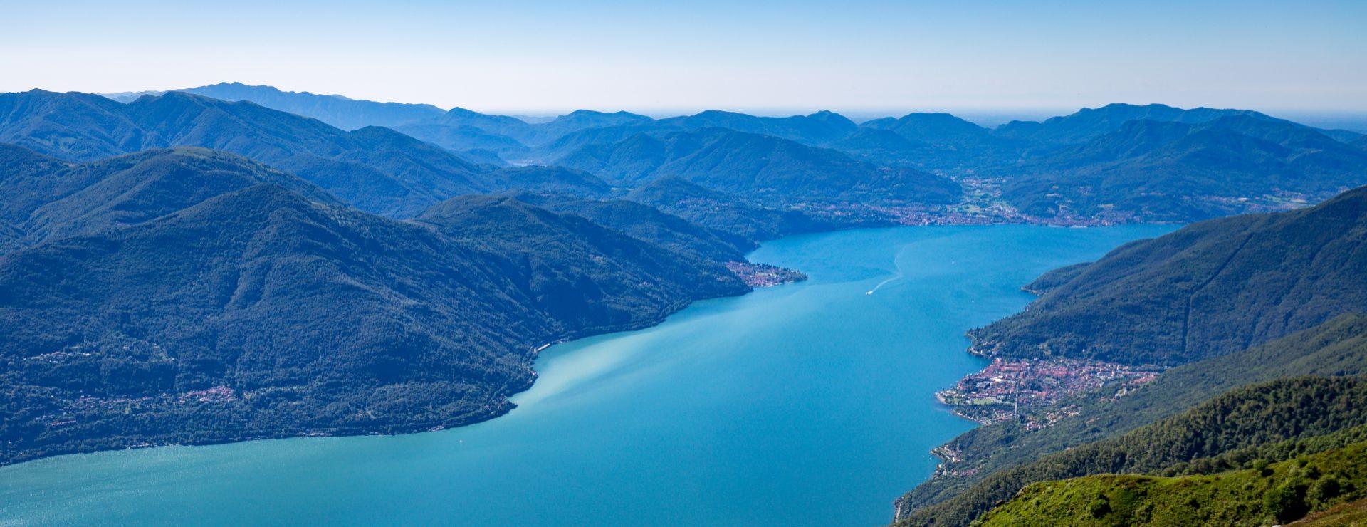 Panorama di un lago circondato da montagne verdi e cielo limpido.