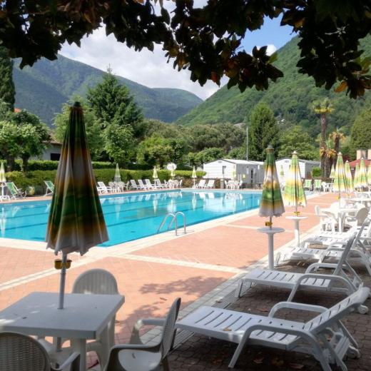 Piscina all'aperto circondata da montagne, con lettini e ombrelloni colorati.