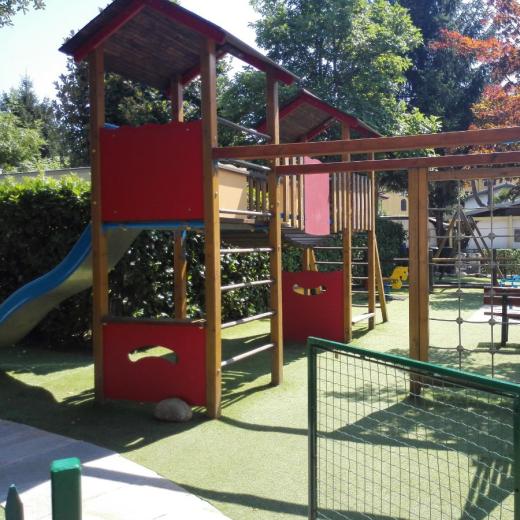 Parco giochi con scivolo, strutture in legno e pavimento in erba sintetica.