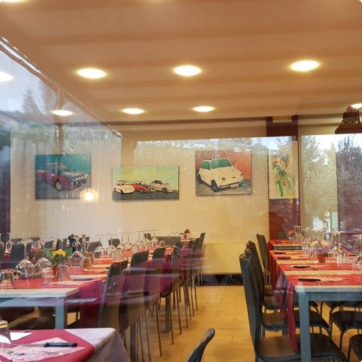 Ristorante con tavoli apparecchiati e quadri di auto alle pareti.